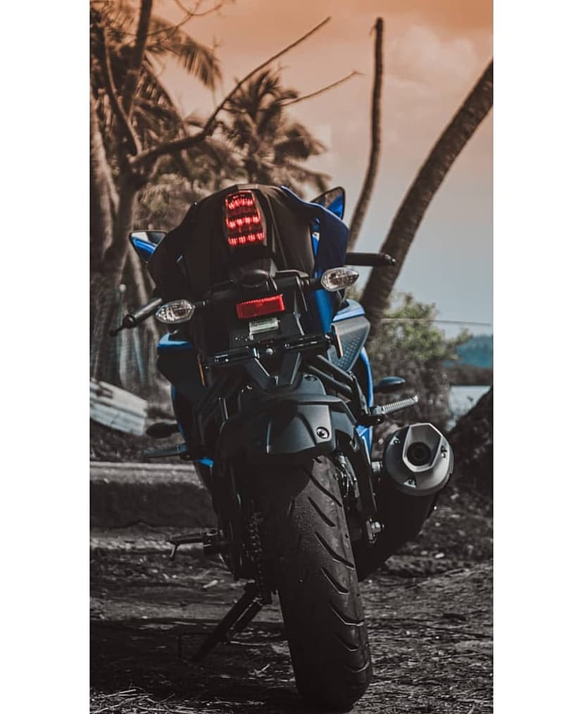 Blue motorcycle tail lights and rear tire sit before silhouetted palm trees under a warm tropical sky.