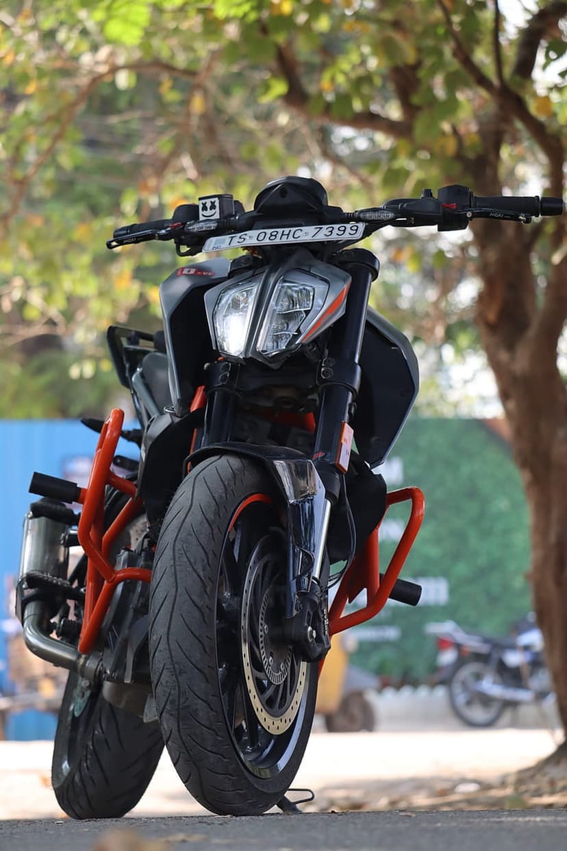 KTM Duke motorcycle with orange crash bars and custom exhaust parked against a blurred green park background.