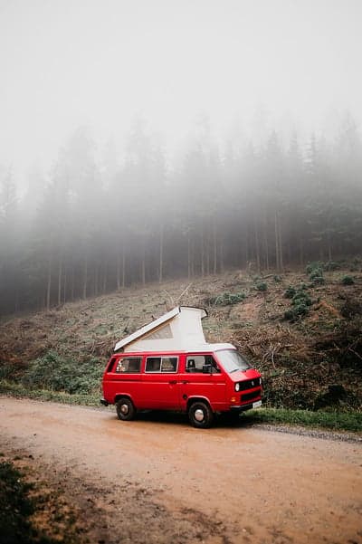Red camper van parked on dirt road in foggy forest