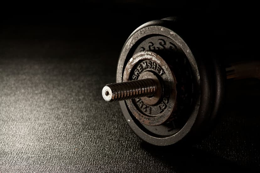 Textured iron weight plate on a dumbbell with a metallic sheen against a dark, minimalist background.