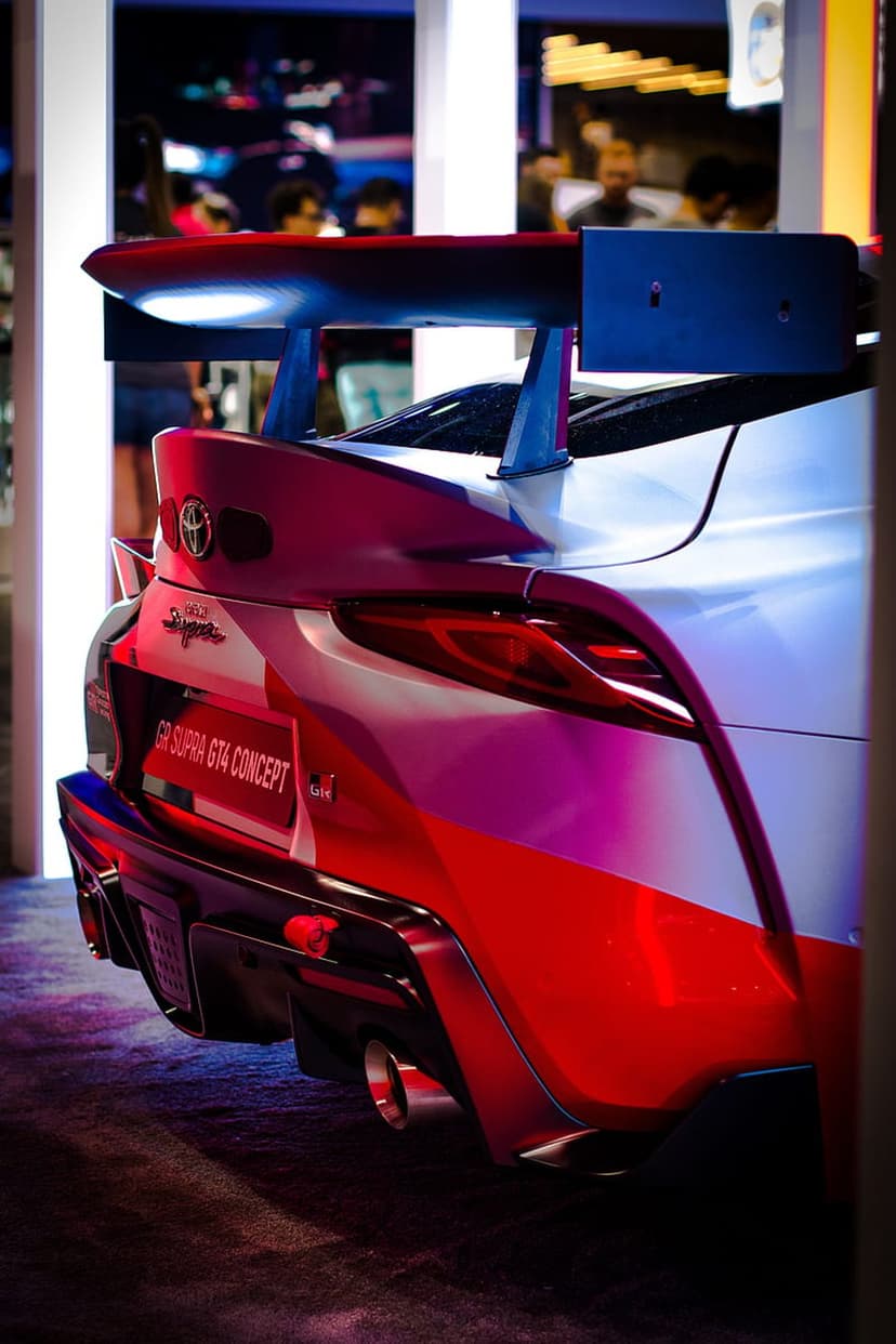 Red Toyota Supra GT4 concept car rear wing and taillights showing metallic paint and aerodynamic diffuser.