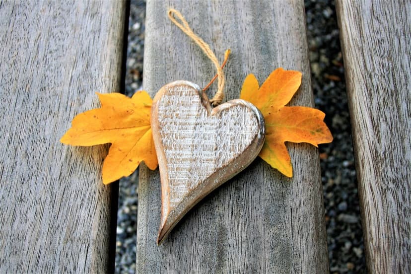 Distressed wooden heart with twine string resting on weathered planks surrounded by bright yellow autumn leaves.
