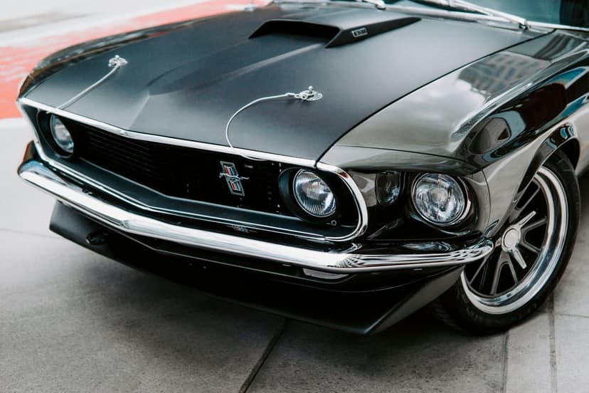 Classic black Ford Mustang front end showing a chrome pony emblem, mesh grille, dual headlights, and hood scoop.
