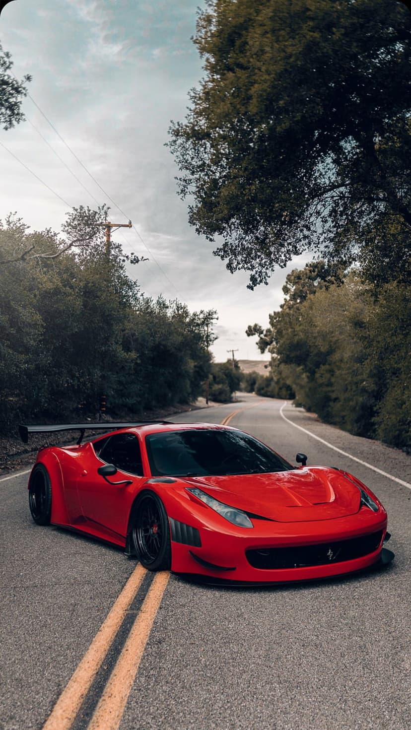 Red Ferrari supercar with a large rear spoiler parked on a winding asphalt road through a dense green forest.