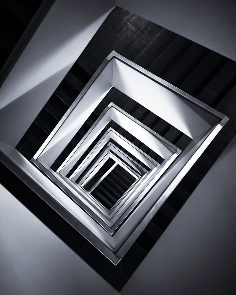 Square metallic railings form a receding geometric pattern with harsh light and dark shadows in a deep stairwell.