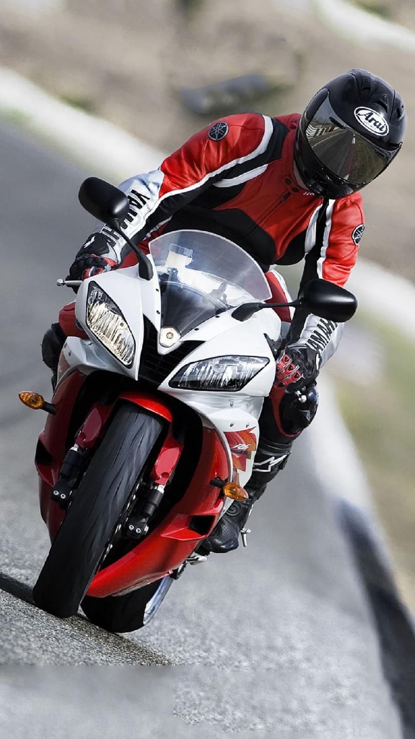 Motorcyclist in a red racing suit leans a sportbike deep into a turn on a textured asphalt racetrack.