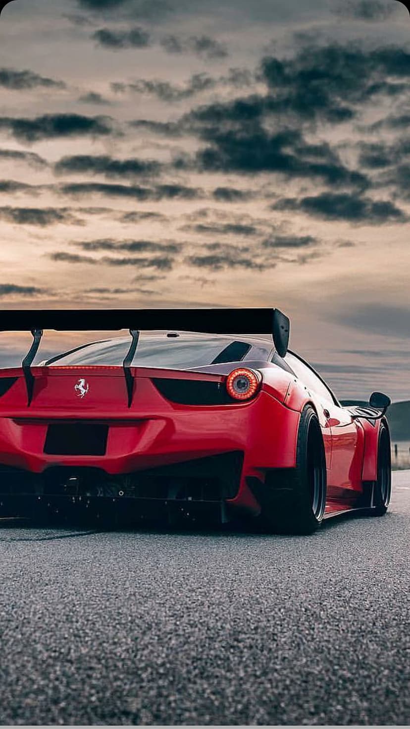 Ferrari 458 Italia GT race car with a large rear wing parked on a track under a dramatic, cloudy grey sky.