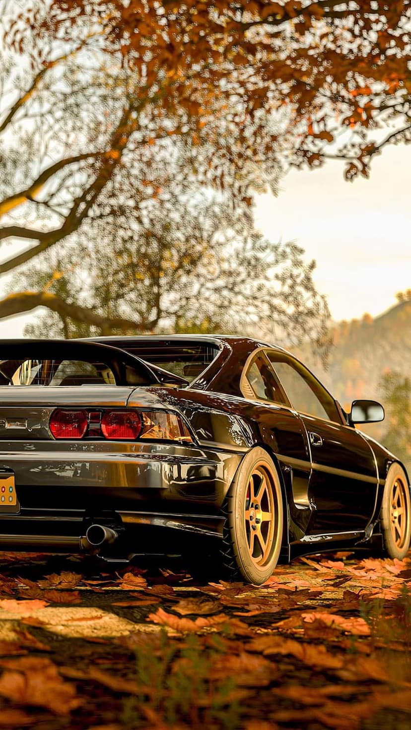 Black Toyota MR2 sports car on a road scattered with orange maple leaves during a sunny autumn afternoon.