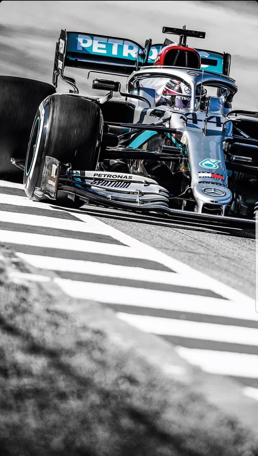 Formula 1 race car with visible Petronas logos speeds on a track in a grainy monochrome close-up motion shot.
