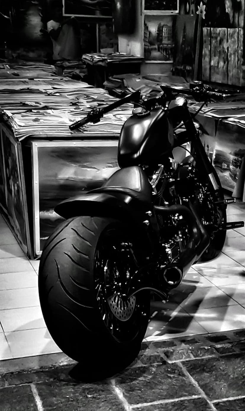 Custom chopper motorcycle with a wide rear tire parked inside a monochrome art studio filled with canvases.