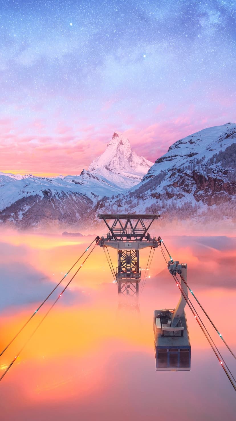 Gondola lift hanging over orange clouds with jagged snow-covered mountains under a starry twilight sky.