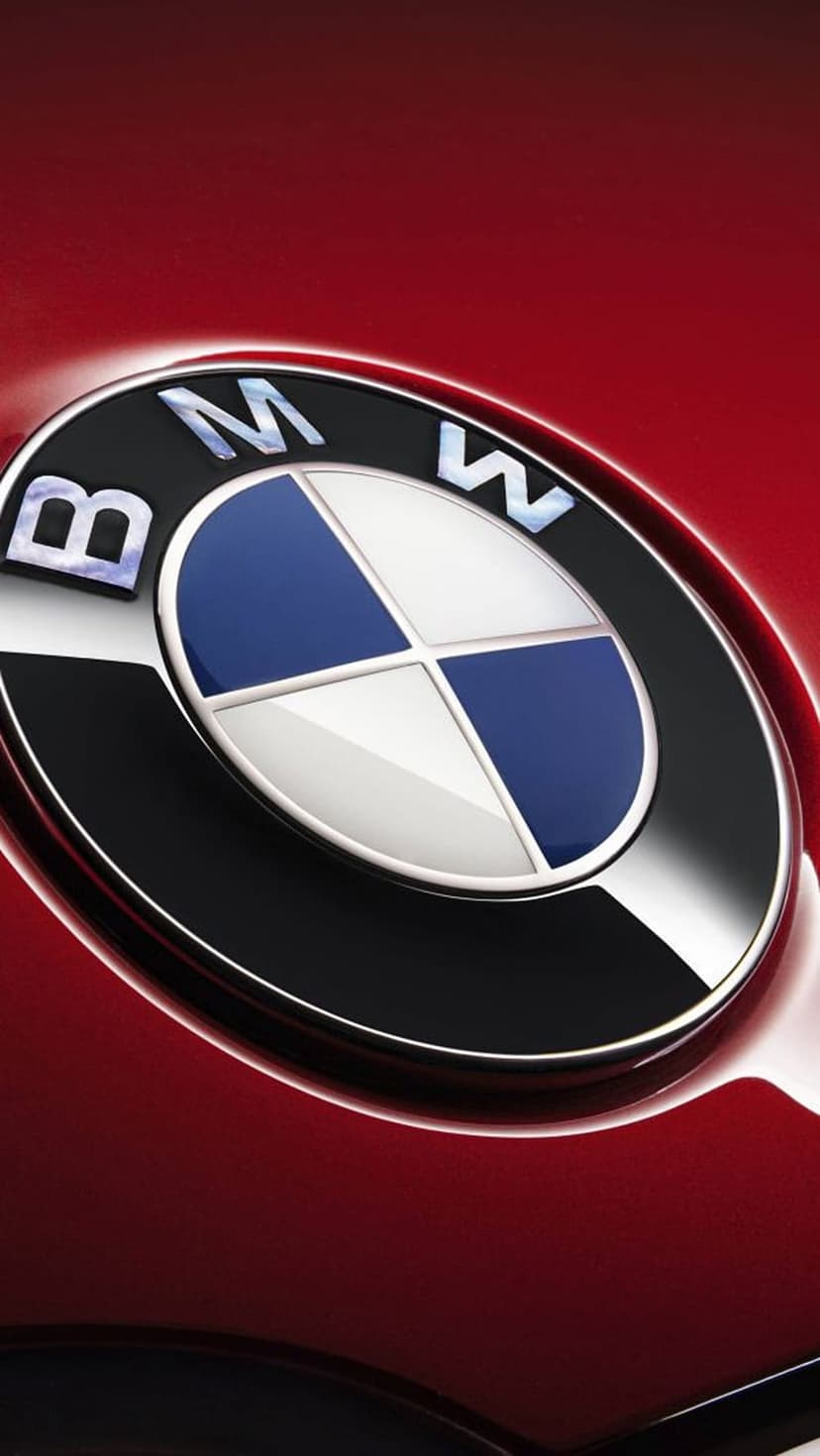 BMW logo emblem featuring blue and white quadrants on a glossy red car body with chrome metallic reflections.