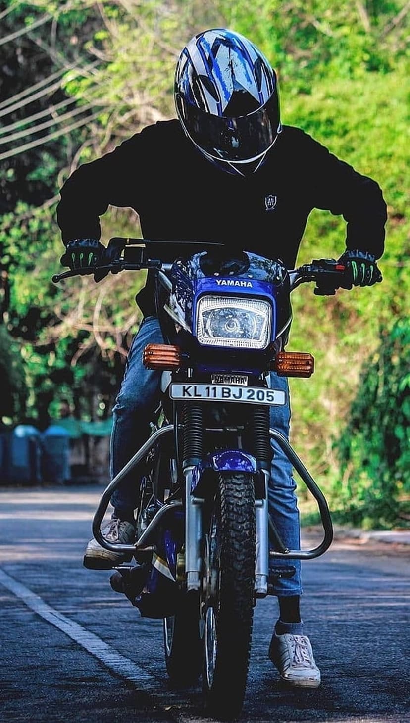 Motorcyclist in a blue helmet riding a blue Yamaha sportbike on a paved road surrounded by dense green forest.