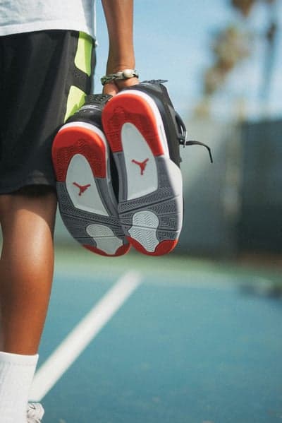 Person holds Jordan sneakers on a tennis court