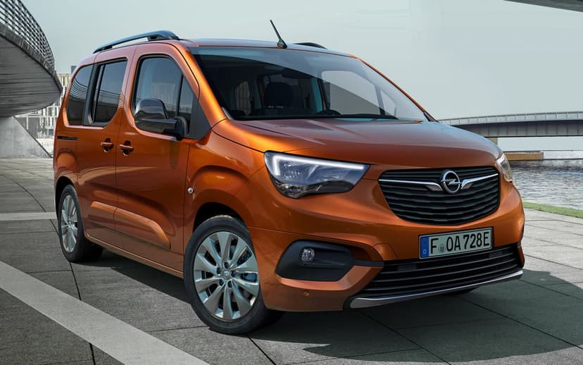 Metallic orange Opel Combo-e Life electric van parked on a concrete waterfront promenade under a clear sky.