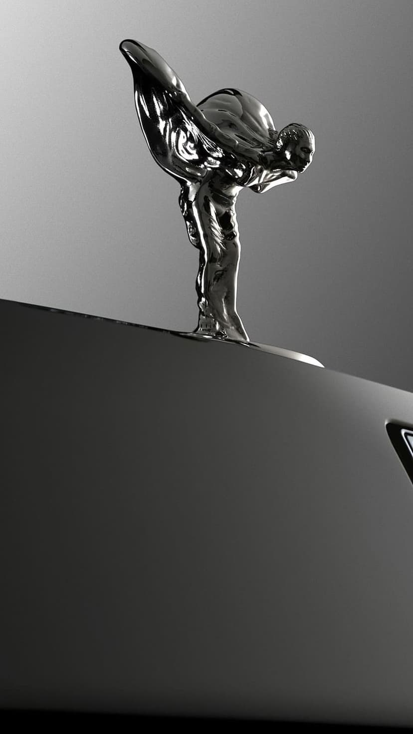 Spirit of Ecstasy chrome sculpture with outstretched wings on a dark car hood in a monochrome close-up shot.