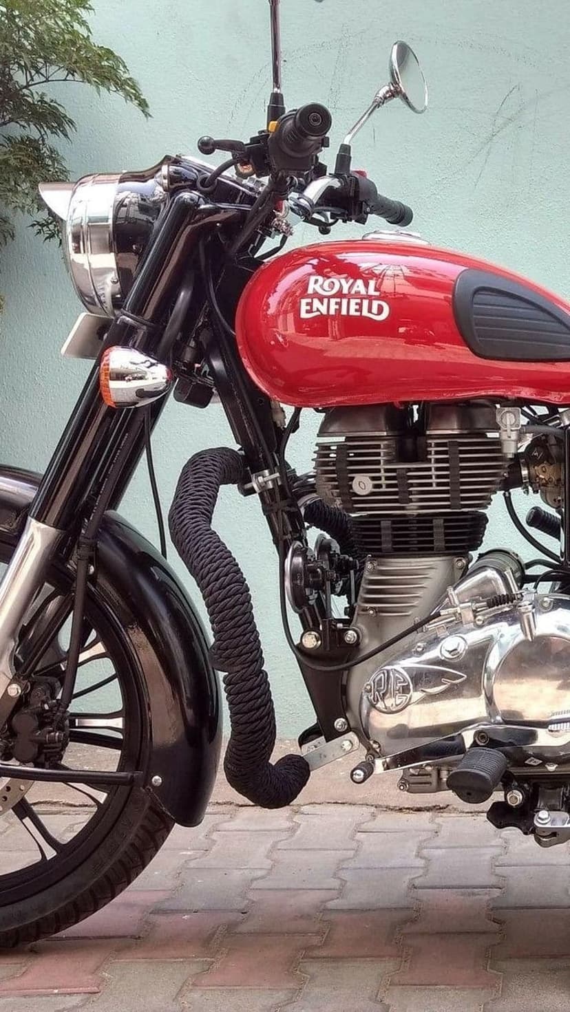 Red Royal Enfield motorcycle fuel tank and chrome engine components against a teal wall in vertical view.