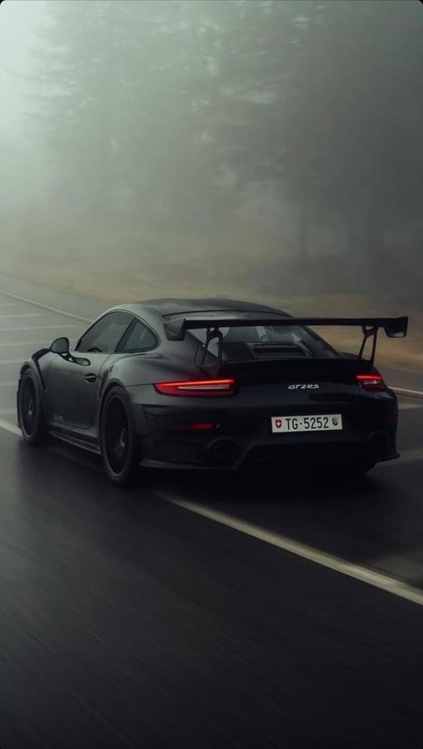 Porsche 911 GT2 RS rear view on a wet forest road with red taillights glowing through heavy morning fog.