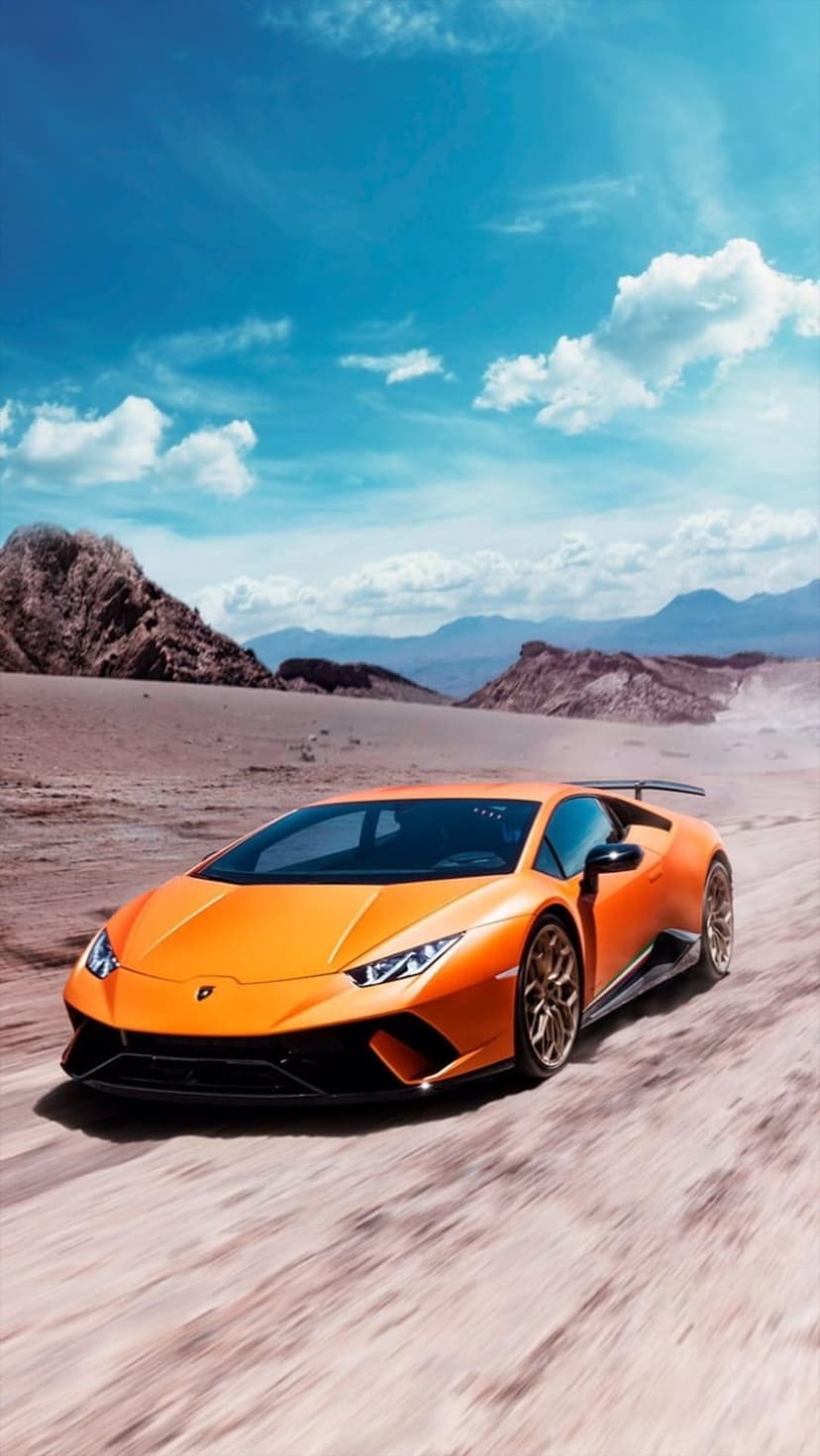 Orange Lamborghini supercar kicks up dust while racing through a sunny desert landscape under a blue cloud sky.