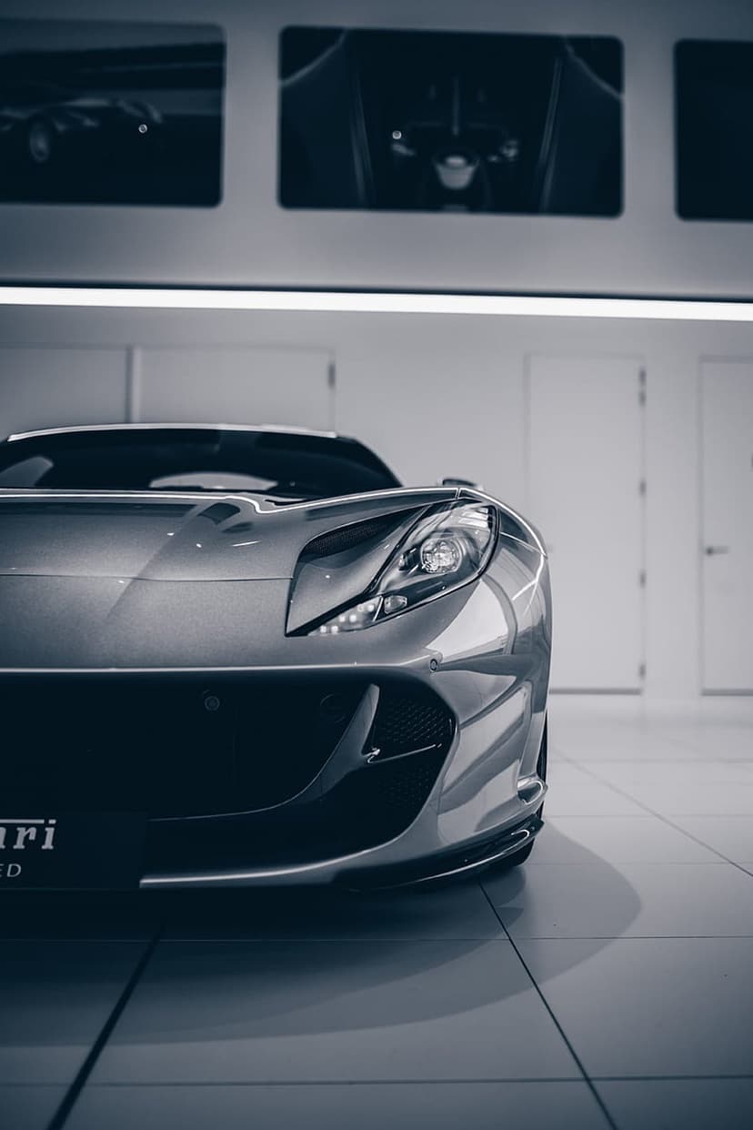 Silver Ferrari front end with aggressive headlights parked in a bright showroom with white doors and sleek floors.