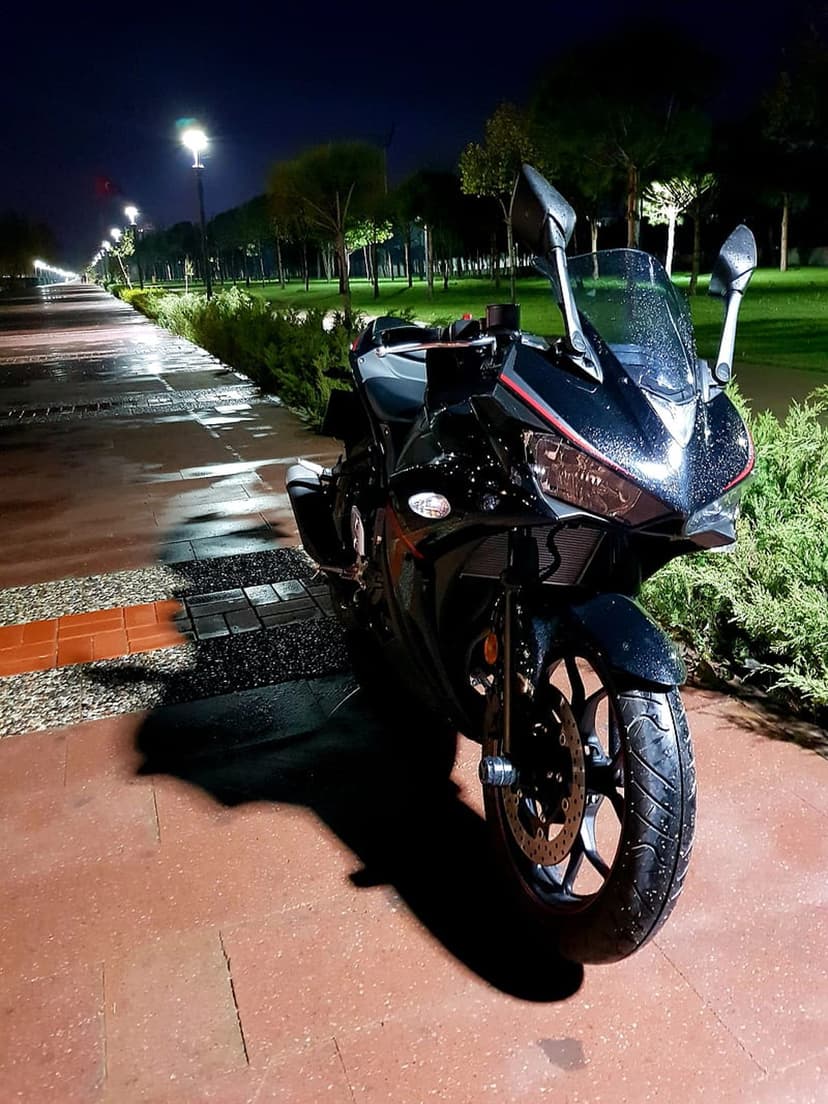 Black sport motorcycle parked on a wet stone path at night with streetlights reflecting in rain puddles.