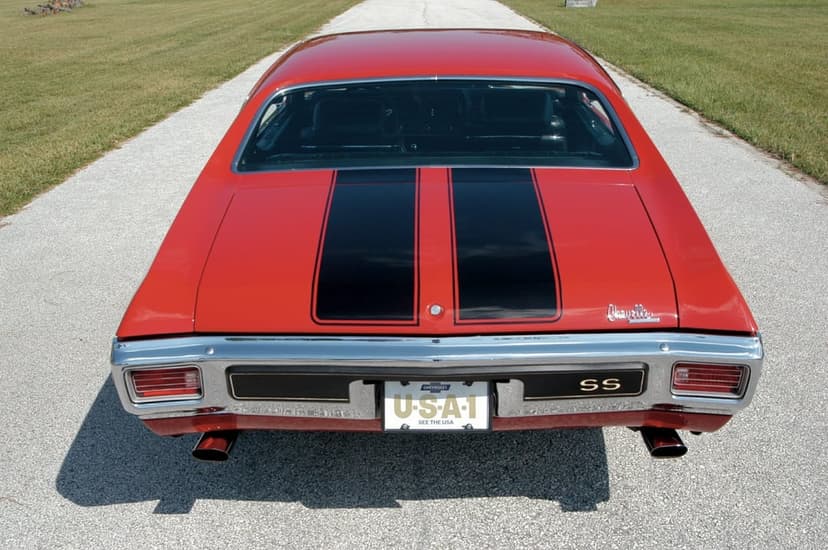 Red 1970 Chevrolet Chevelle SS with black racing stripes and chrome bumper on an asphalt driveway.