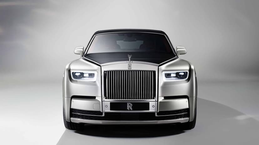 Front view of a silver and black luxury sedan with a chrome grille and Spirit of Ecstasy emblem in a studio.