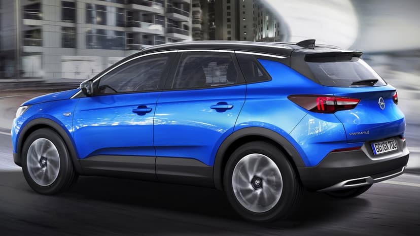 Blue Opel Grandland X SUV with a black roof driving on a city road with motion blur and modern buildings.