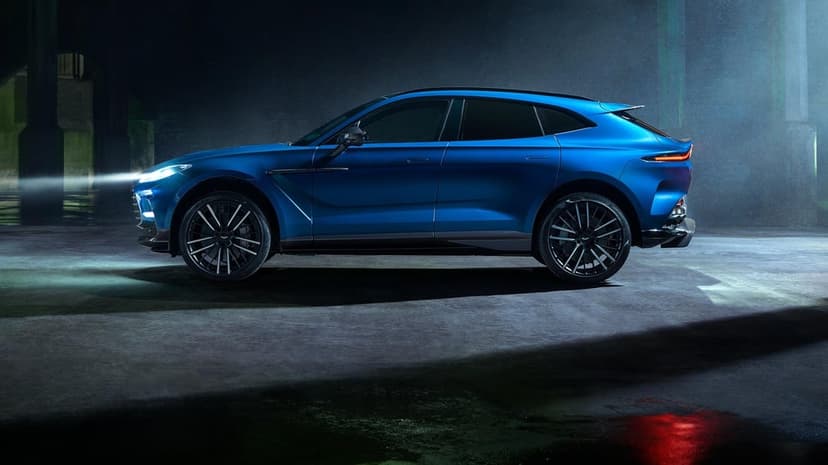 Side view of a blue luxury SUV with glowing headlights in a dark atmospheric industrial garage setting.