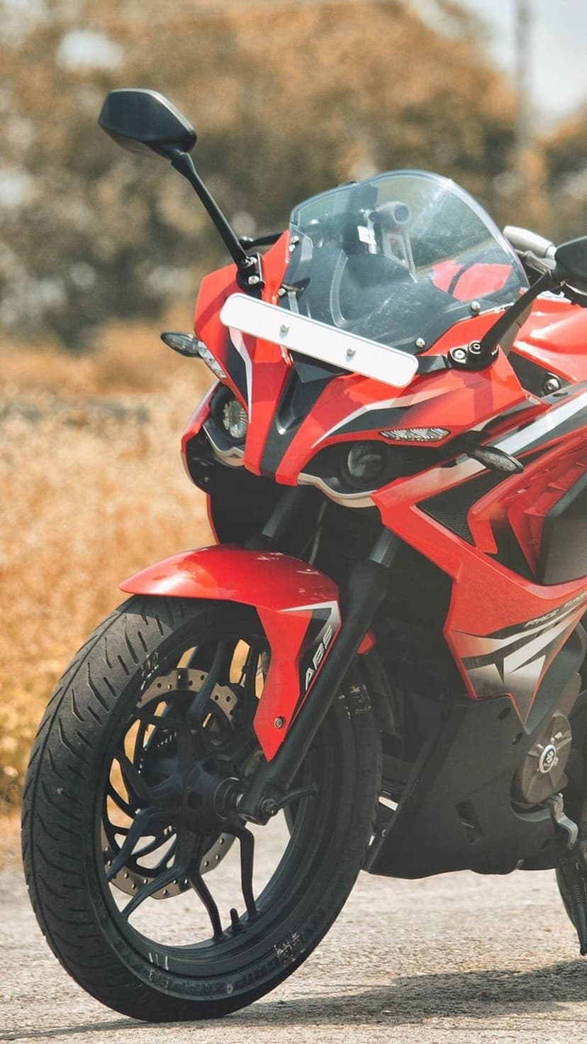 Red sports motorcycle front view with a black windshield and alloy rims against a blurred grassy background.