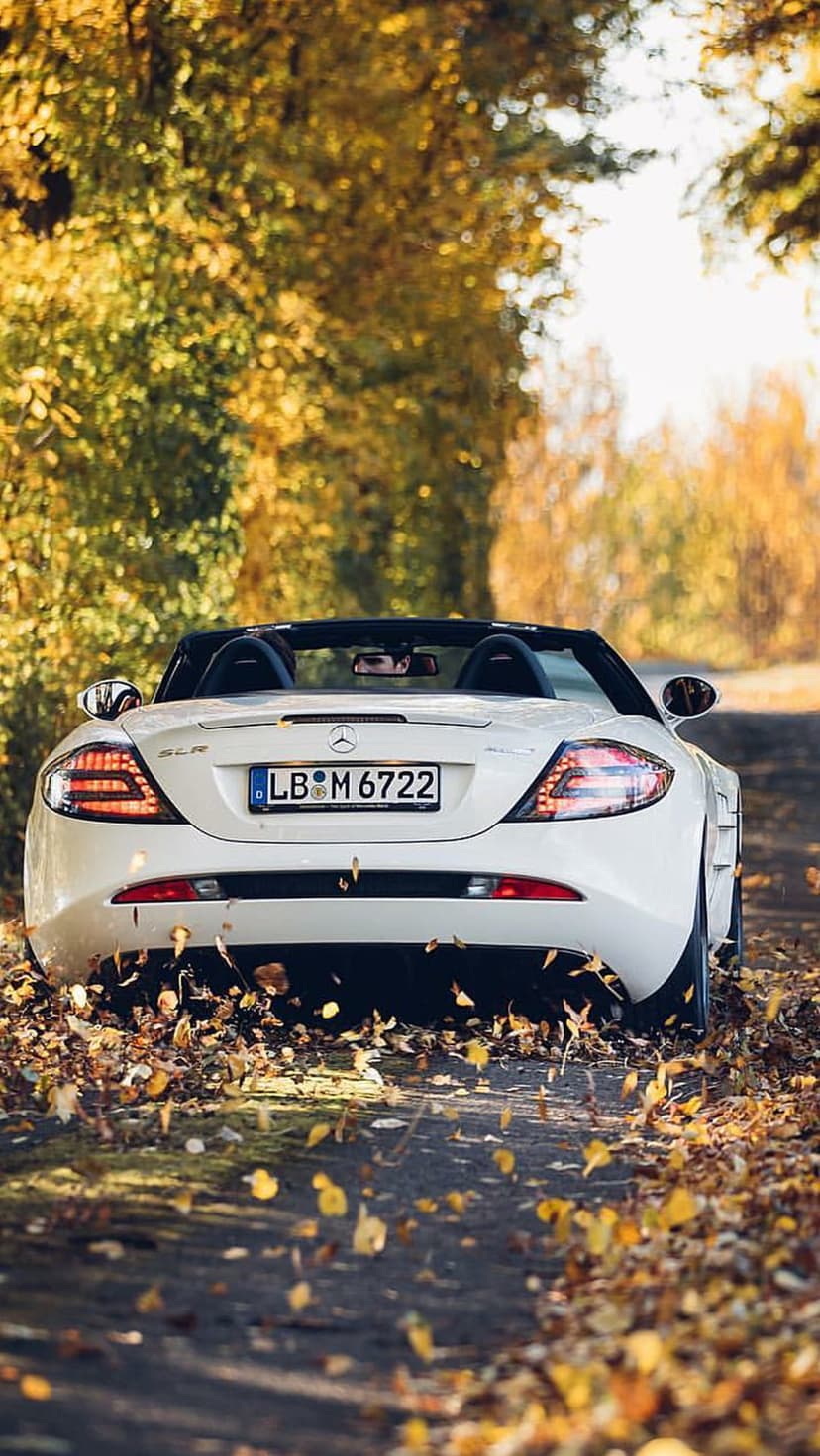White Mercedes-Benz SLR McLaren convertible parked on a road covered in yellow and orange autumn leaves.