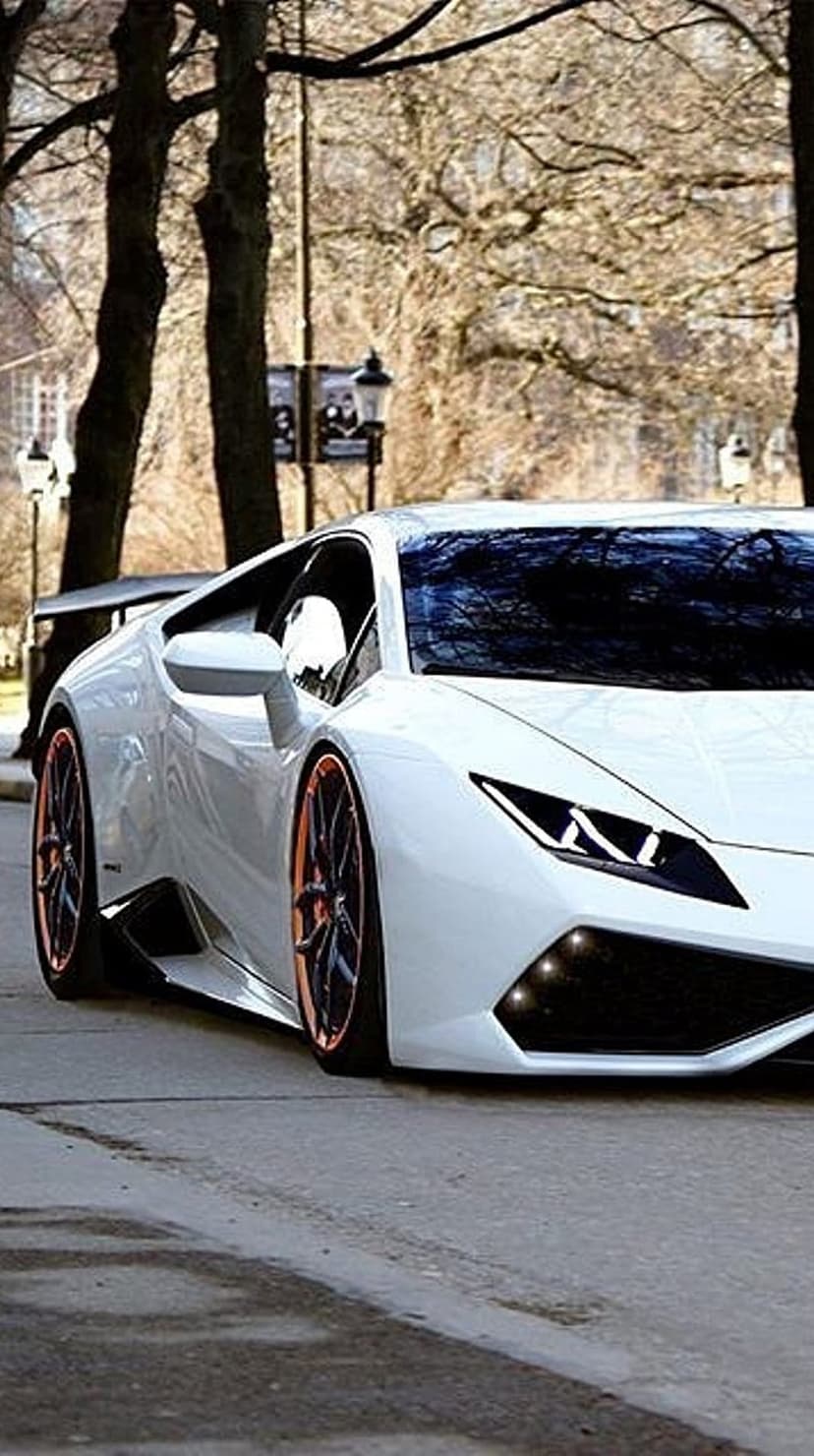White Lamborghini Huracan parked on a wet street at night with glowing headlights and orange-trimmed wheels.