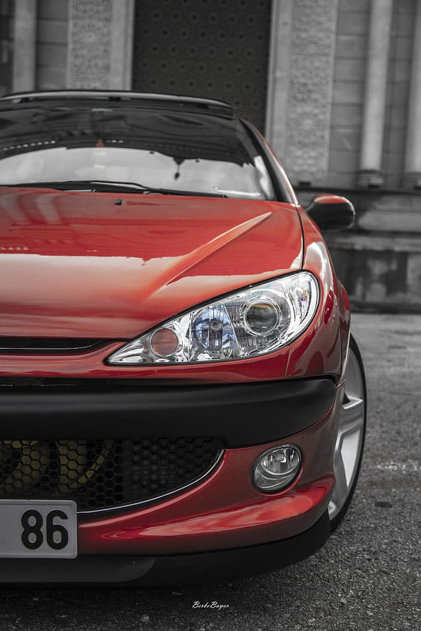 Red car front with sharp headlights, black honeycomb grille, and license plate 86 against a grey background.