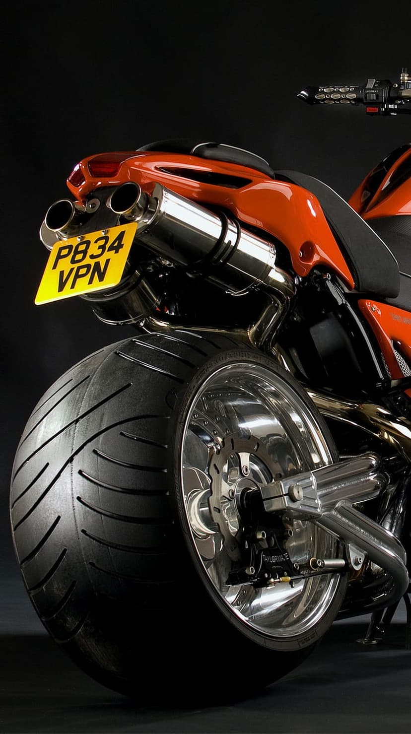 Orange motorcycle rear tire and dual chrome exhaust pipes with a yellow license plate on a modern sportbike.