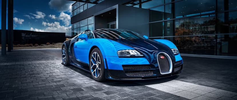 Blue and black Bugatti Veyron supercar parked on stone pavement in front of a modern glass office building.