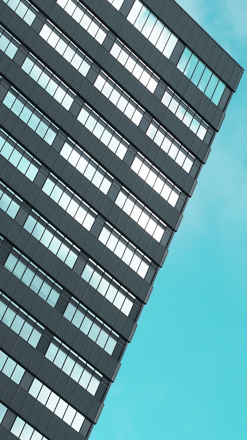 Reflective glass skyscraper windows meet at a sharp angle against a vivid clear blue sky in bright daylight.