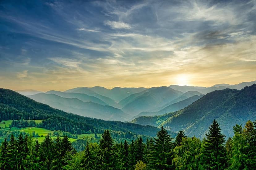 Layers of green forested mountains rise through morning mist as golden sunlight illuminates the hazy valley.