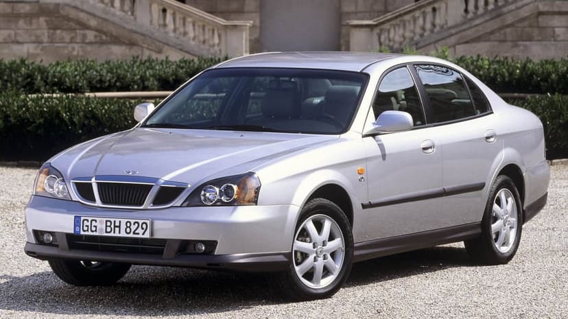 Silver Daewoo Magnus sedan parked on a gravel path with classical stone stairs and green hedges in the background.