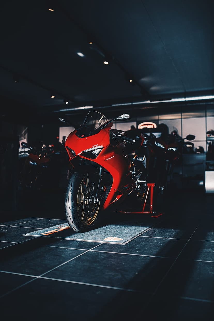 Red Ducati sportbike with aerodynamic fairings displayed under spotlights in a dark, luxury showroom setting.