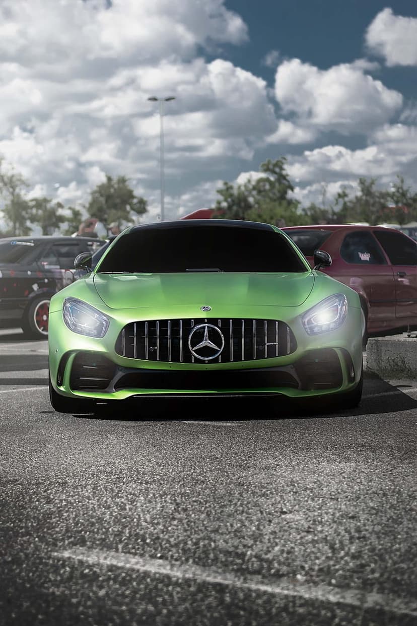 Green Mercedes-AMG GT with a vertical grille and LED headlights parked on asphalt against a cloudy sky backdrop.