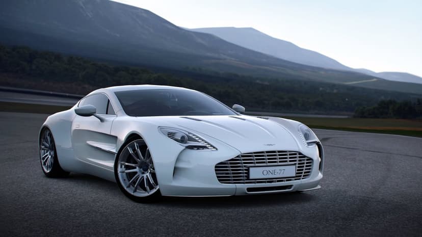 White Aston Martin One-77 supercar on an asphalt track with misty mountains and hills in the soft background light.