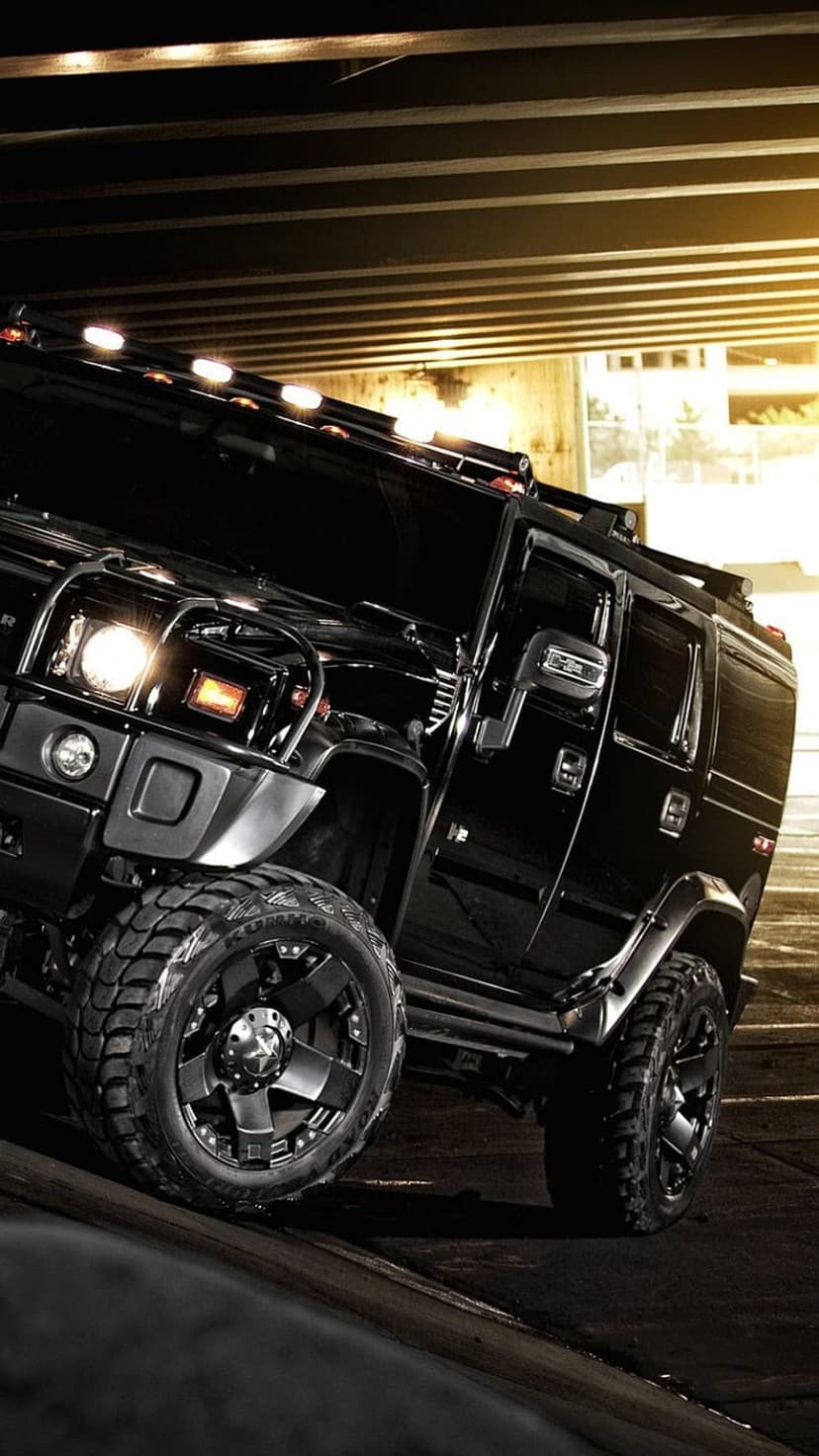 Hummer H2 tire and undercarriage with deep tread grooves and mechanical suspension parts under bright lights.