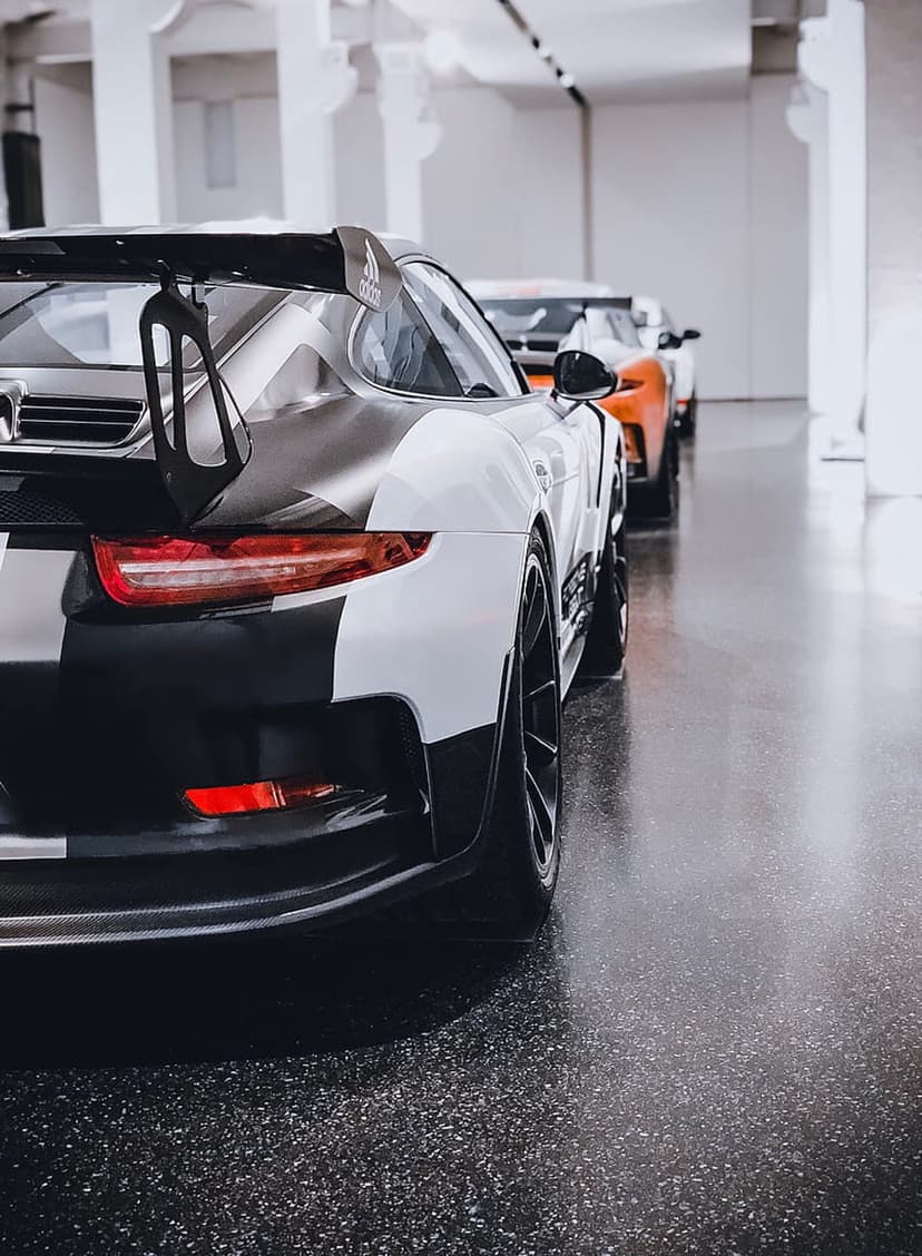 Porsche GT3 RS with black and white racing stripes, a large rear wing, and wide tires in a luxury showroom.