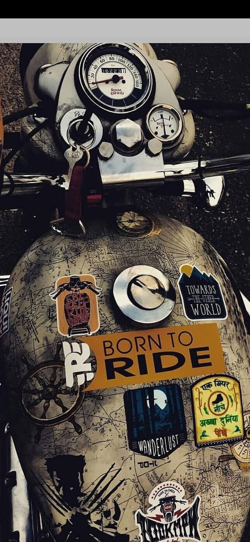 Vintage motorcycle fuel tank featuring a cartographic map decal and various colorful adventure-themed stickers.