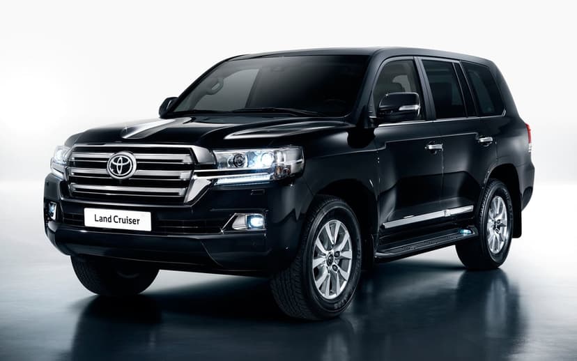 Black Toyota Land Cruiser SUV with glowing LED headlights in a clean white studio with a reflective floor.