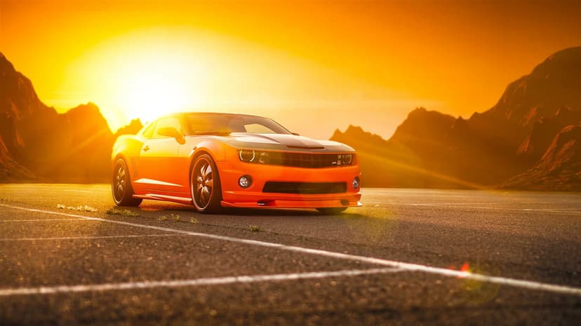 Orange Chevrolet Camaro SS muscle car parked on asphalt against a mountain backdrop during a golden sunset.
