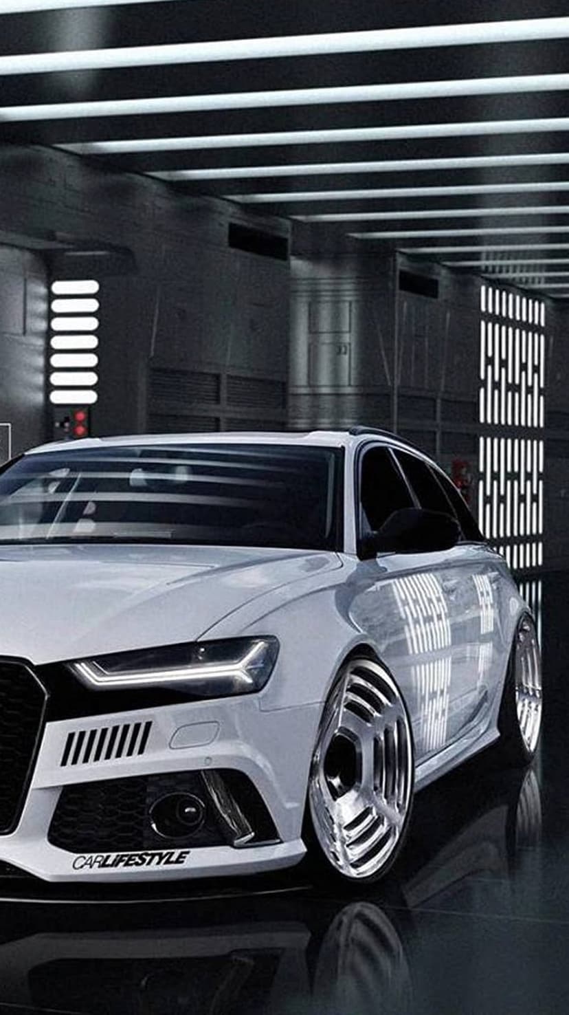 White Audi sedan with glowing LED headlights and polished chrome wheels parked in a dark industrial garage.