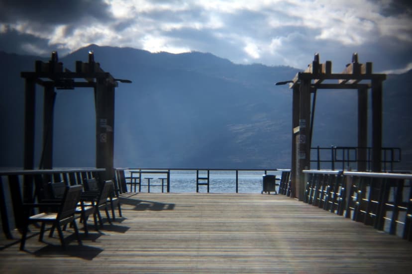 Wooden chairs on a lake pier facing misty mountains under heavy clouds in a vertical scenic view.
