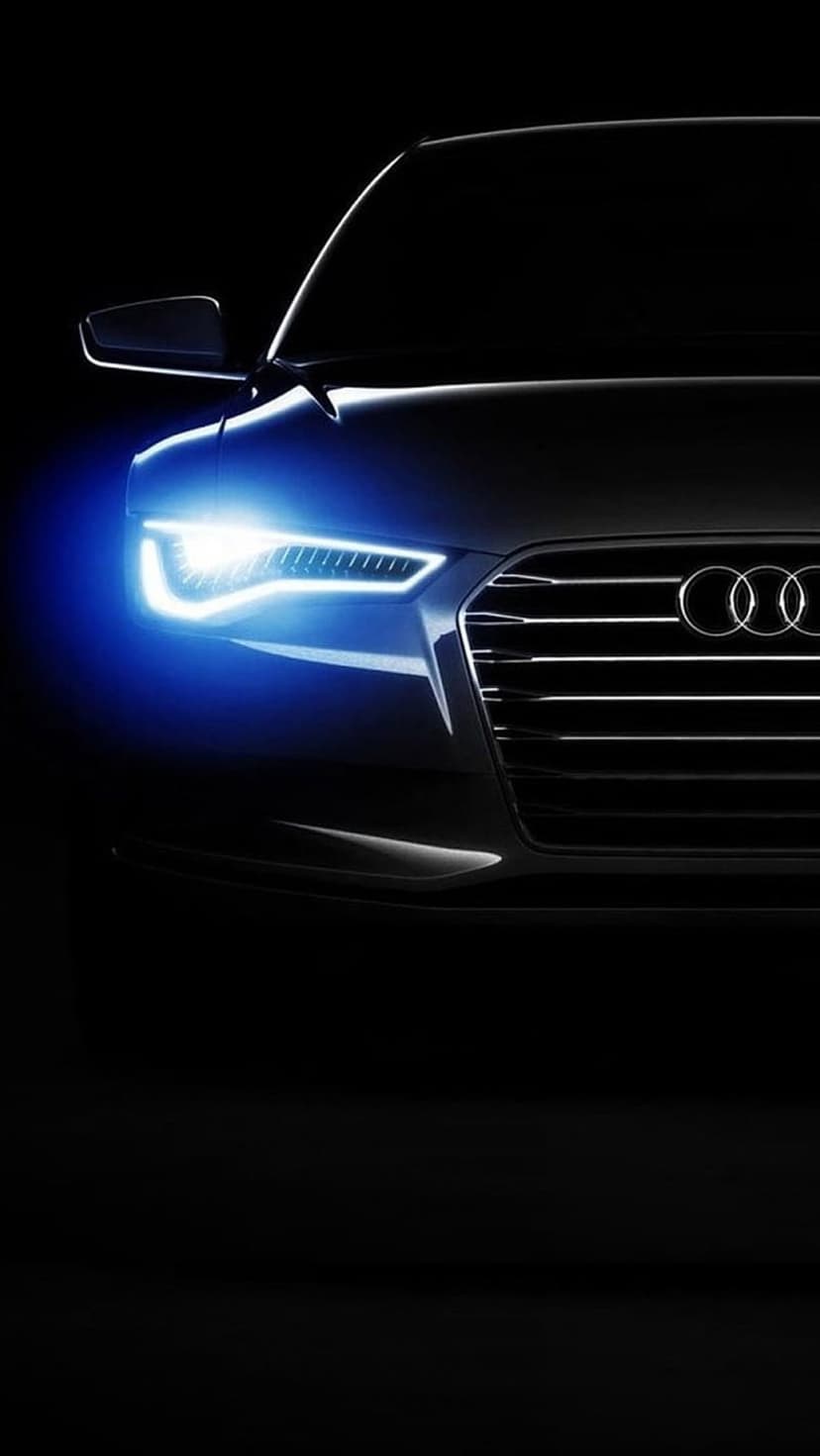 Audi car front grille and logo illuminated by neon blue LED headlights against a dark nighttime background.