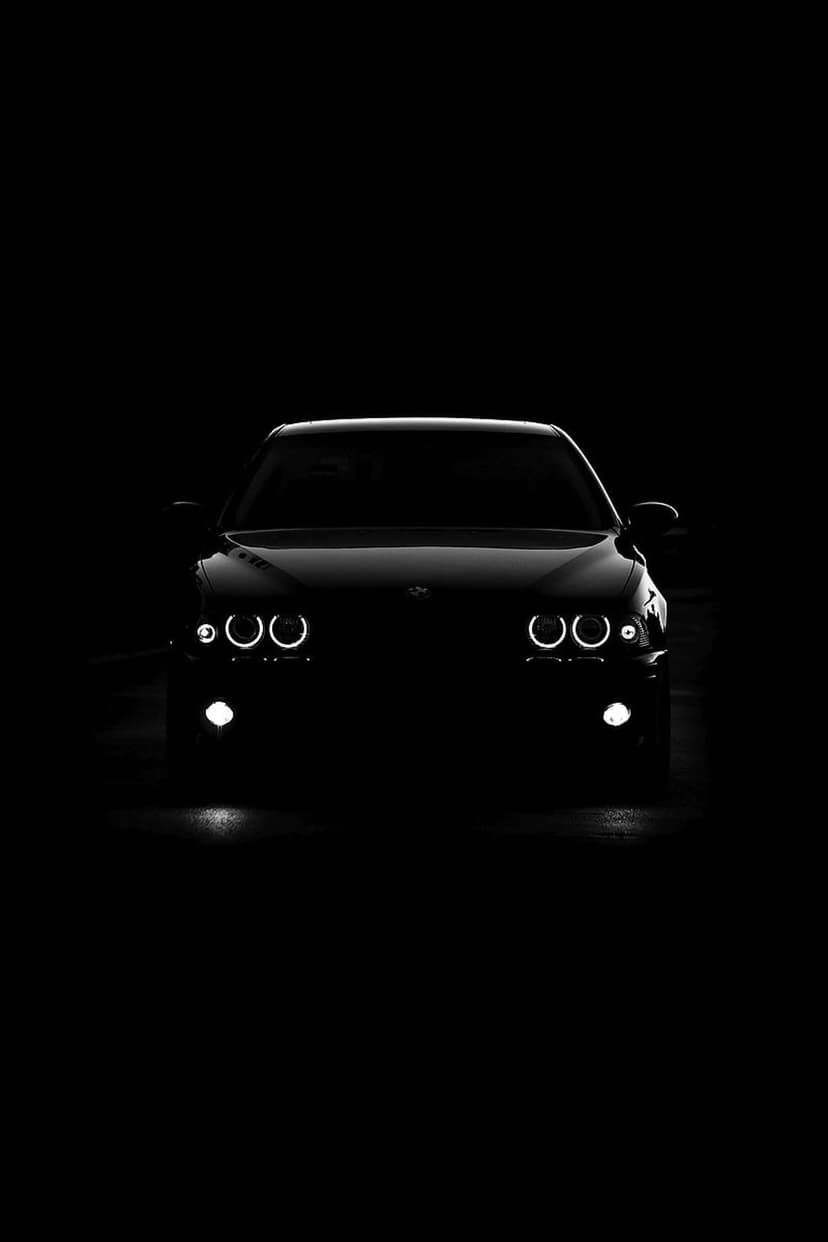 BMW sedan front silhouette with glowing circular LED angel eye headlights against a dark black background.